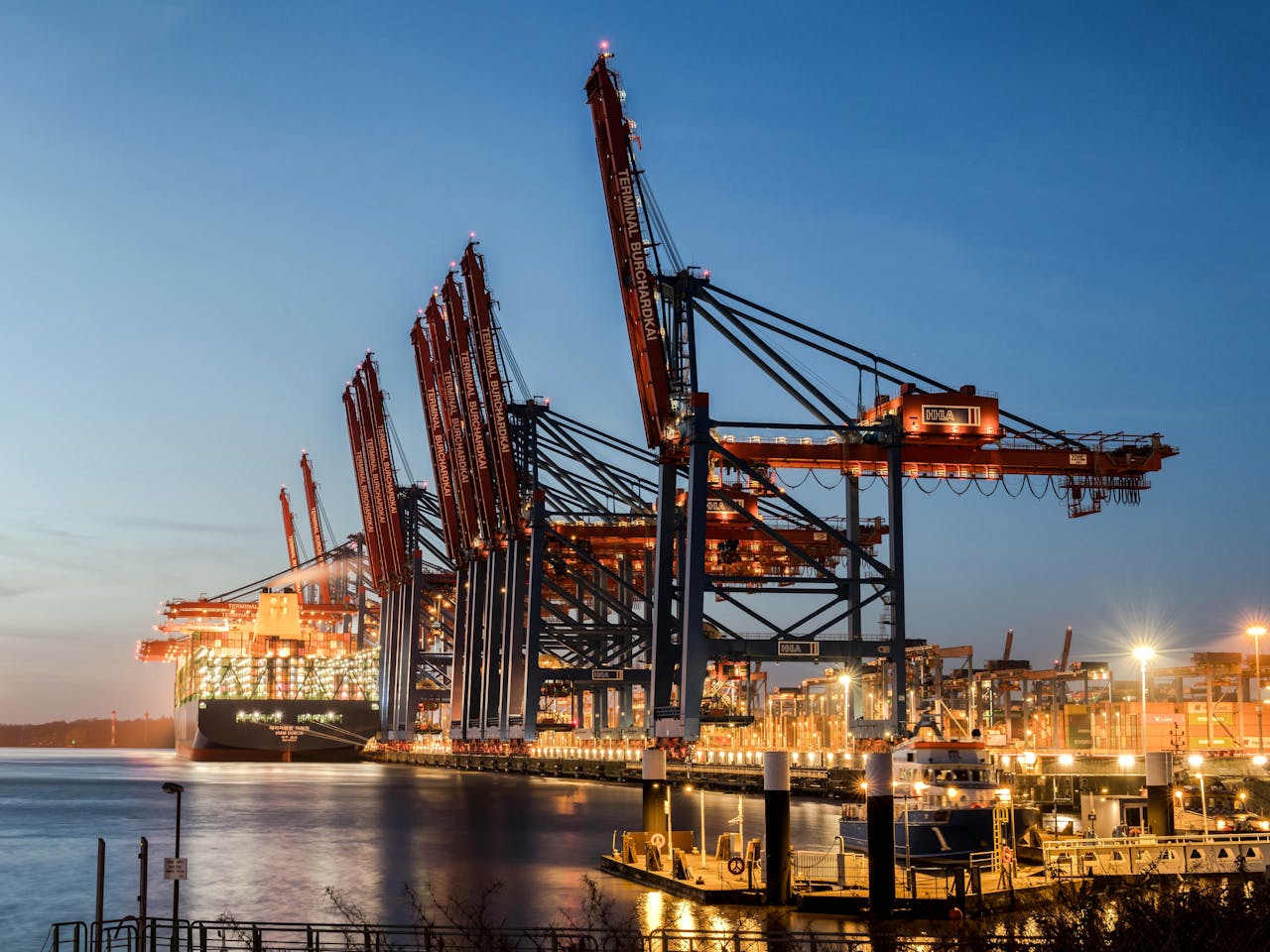 Industrial port scene at Hamburg with illuminated cranes and container ships during dusk.